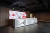 Стойка ресепшн РИ-136 с LED-подсветкой 12V в тёмном интерьере, белая глянцевая.